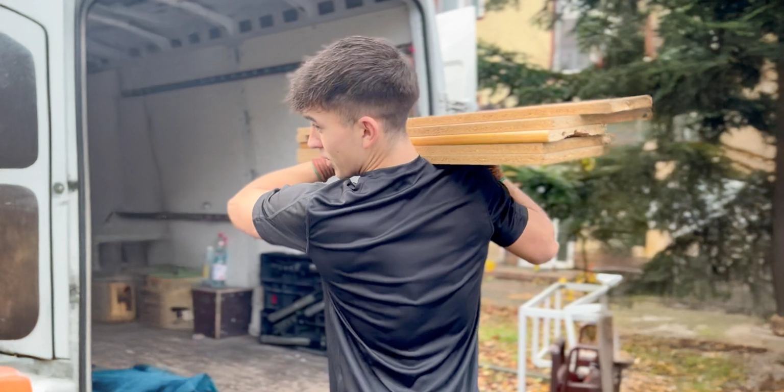Alles4You-Mitarbeiter trägt demontierte Möbelteile auf der Schulter zum offenen Transporter bei einem Umzug in Berlin